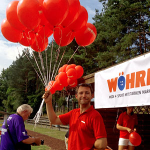 Promoter hält sehr viele rote Luftballons in der Hand.