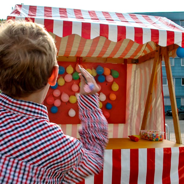 Junge wirft Dart in Richtung einer Marktbude mit Luftballon-Dartspiel.