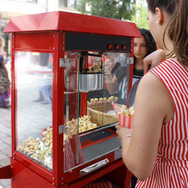 Frau in rot-weiß gestreiftem Kleid verteilt Popcorn aus einer Retro-Popcornmaschine.