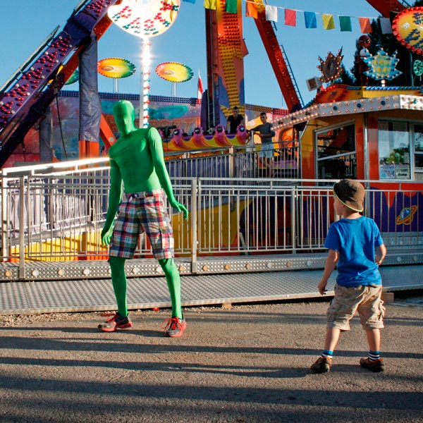 Künstler im grünen Morphsuit steht vor einem  Kind.