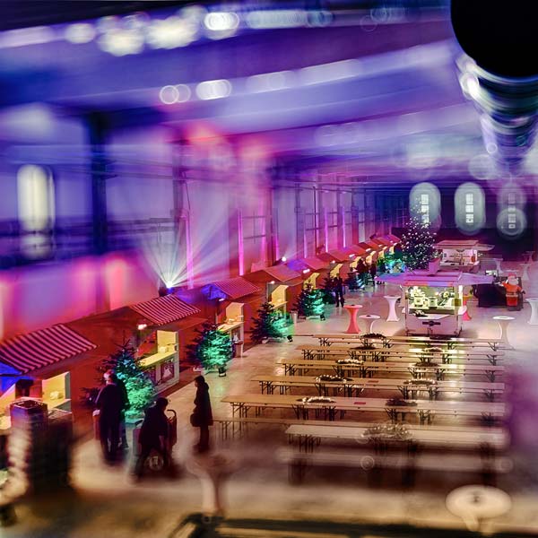 illuminierte Weihnachts-Marktstände in einer Produktionshalle.