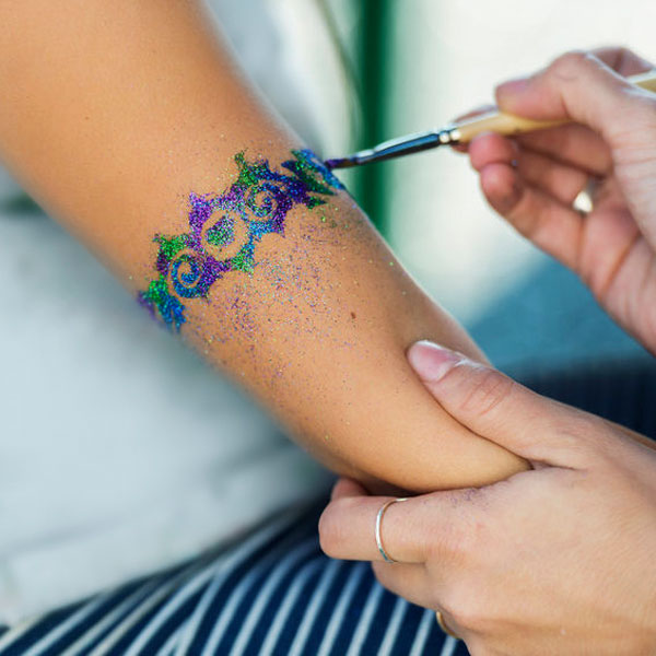Ein Mädchen bekommt ein Glitzer-Tattoo auf den Arm.