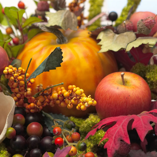 Herbstliche Dekoration mit Kürbis, bunten Blättern und einem Apfel.
