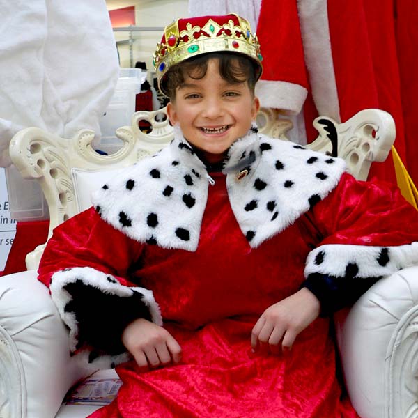 Kind im Königskostüm und Krone wird auf weißem Thron fotografiert.