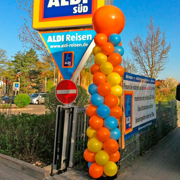 Ballongirlande in orange, gelb und blau an Einfahrt zu Firmengelände von ALDI.