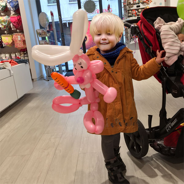 Kleinkind mit Luftballonfigur in Form eines pinken Hasen.