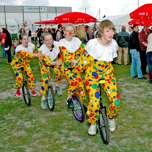 Vier Kinderclowns in gelben Kostümen fahren in einer Reihe auf Einrädern hintereinander her.