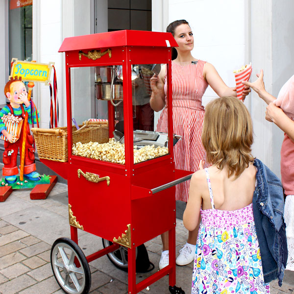 Frau in Retro-Kleid verteilt Popcorn aus Retro-Popcornwagen.