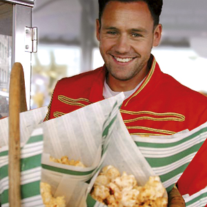 Animateur in Zirkusjacke mit Popcorn in gestreiften Spitztüten.