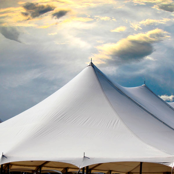 Dach eines weißen Zweimast-Zeltes vor bewölktem Himmel.
