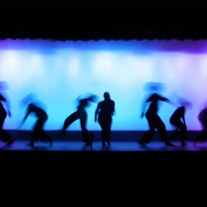 Tänzer auf einer Bühne mit beleuchtetem Hintergrund.