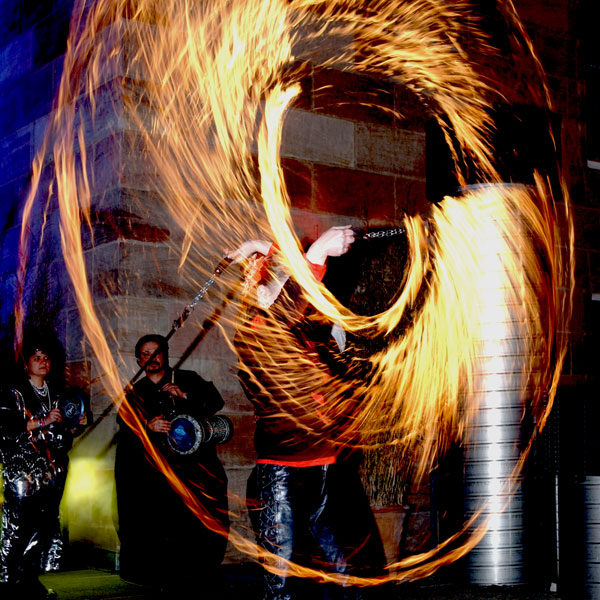 Künstler schwingt brennende Feuerkugeln an Seilen im Kreis.  