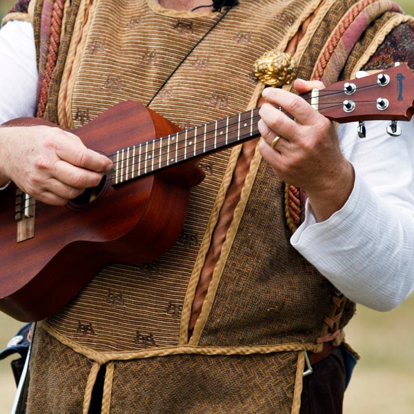 Troubadour im mittelalterlichen Kostüm spielt auf einer Citole/Zupfinstrument.