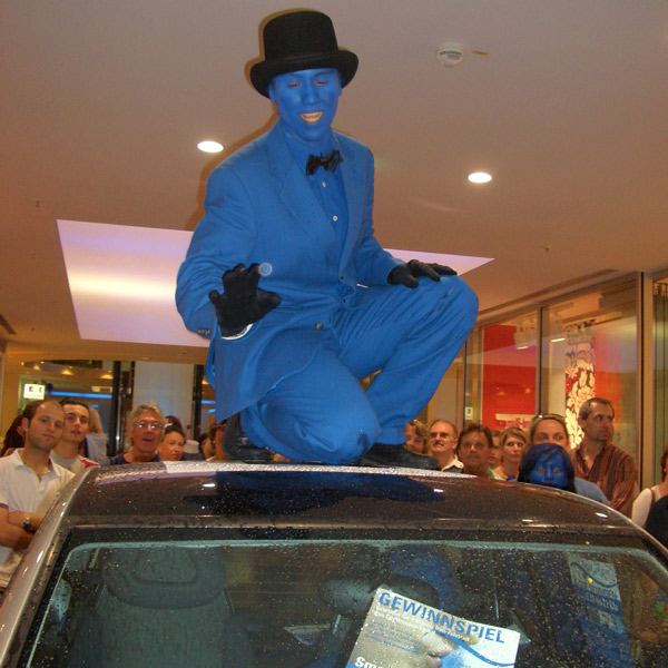 Blauer Colourman sitzt auf Autodach.