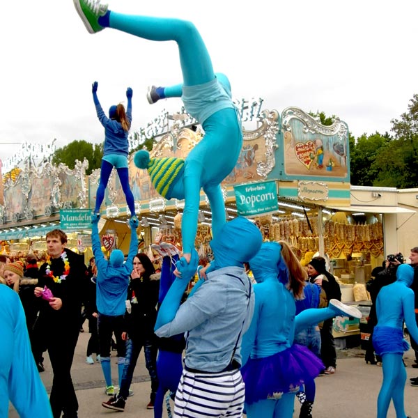 Künstler in blauen Morphsuits zeigen Artistikkünststücke auf Volksfest.