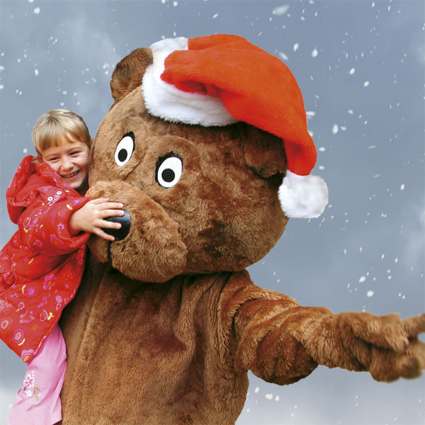 Bär mit Weihnachtsmütze hält Kind auf dem Arm.