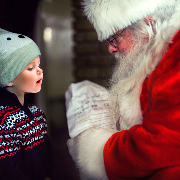 Weihnachtsmann mit kleinem Mädchen liest Wunschzettel.