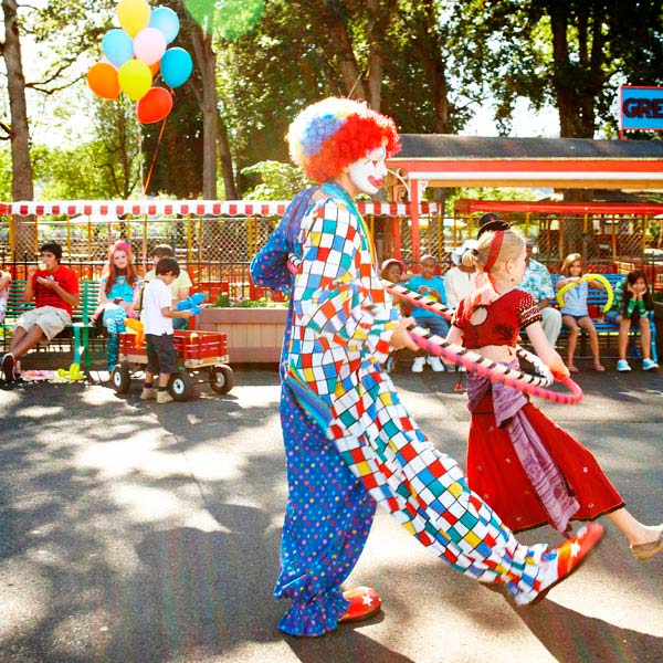 Bunter Clown hält Kind an den Händen und tanzt mit ihm auf der Straße.