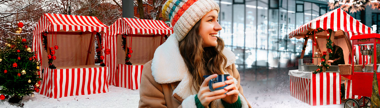 Rotweiß gestreifte Weihnachtsmarktbuden, eine Frau trinkt Glühwein.